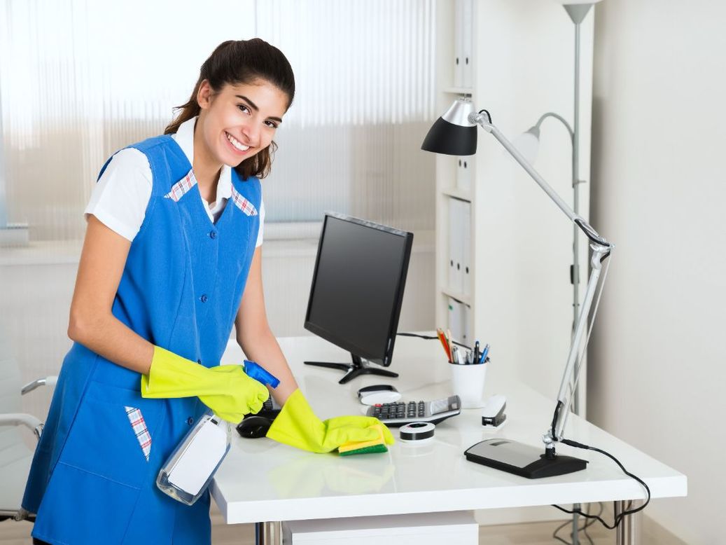 Mujer sonriente, con uniforme de limpieza, limpiando escritorio